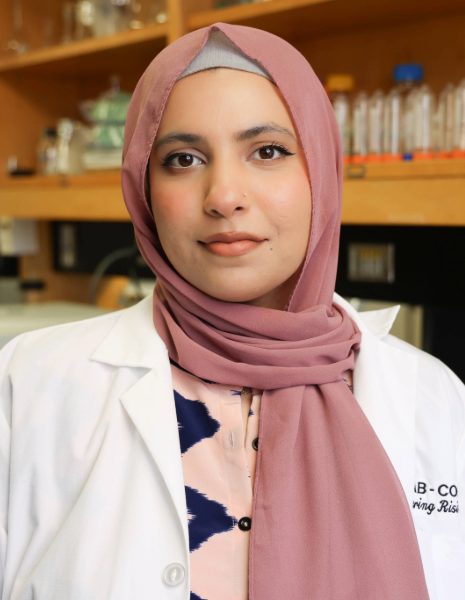 Woman with pink head wrap and nose piercing wearing a white coat in a lab setting